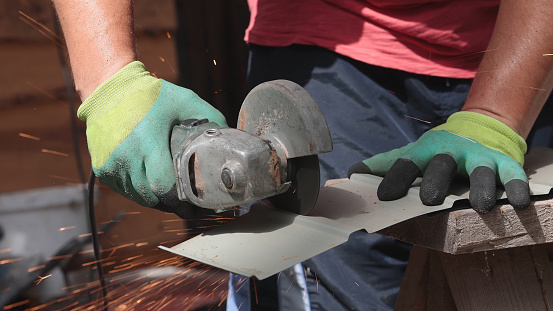 The man cuts a sheet of metal with a manual circular saw. Sparks from cutting metal scatter to the sides.