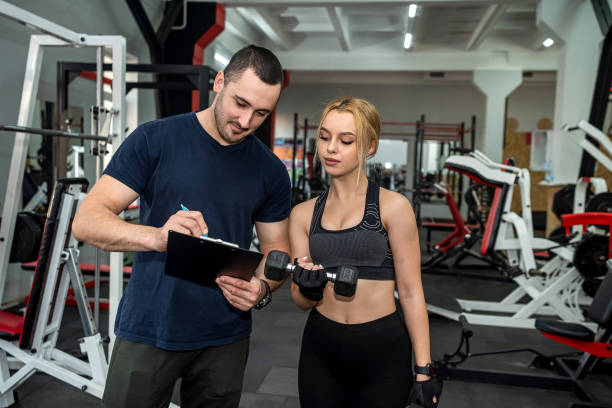 istock personal trainer with slim woman client doing bicep curls working out in gym 1419567039