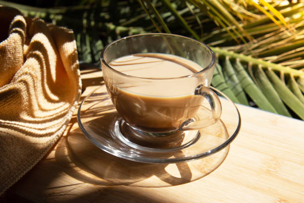 Glass cup with fragrant coffee with contrasting shadows from palm leaves. Close-up