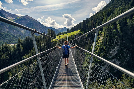 Mother and son are hiking in the Alps - Tyrol, Austria. They are walking on high up suspended bridge over a valley.
Sunny day of summer vacations.
Canon R5