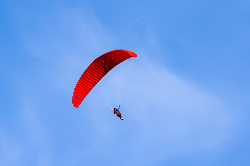 Red and orange paraglider flying in a blue sky.