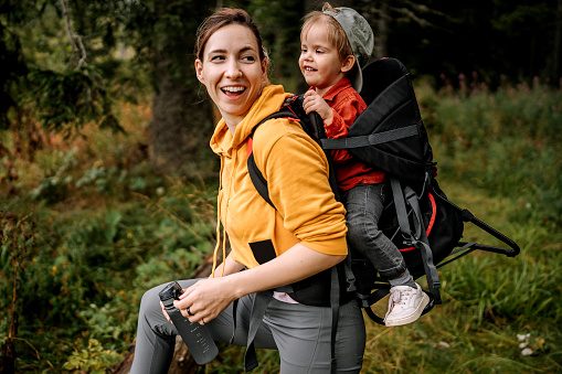 Mom hiking in the forest with her son on her back in a baby carrier