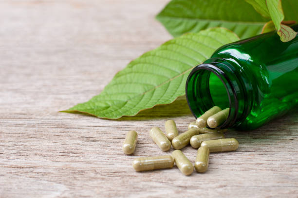 istock Kratom (Mitragyna speciosa) powder capsules pill and green leaf on wood table background. 1419578551