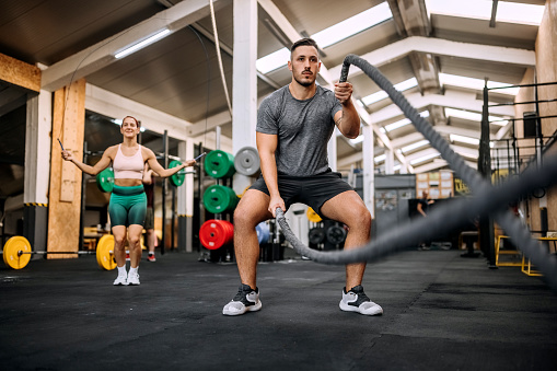 Athletic man focused on fitness training with ropes at gym