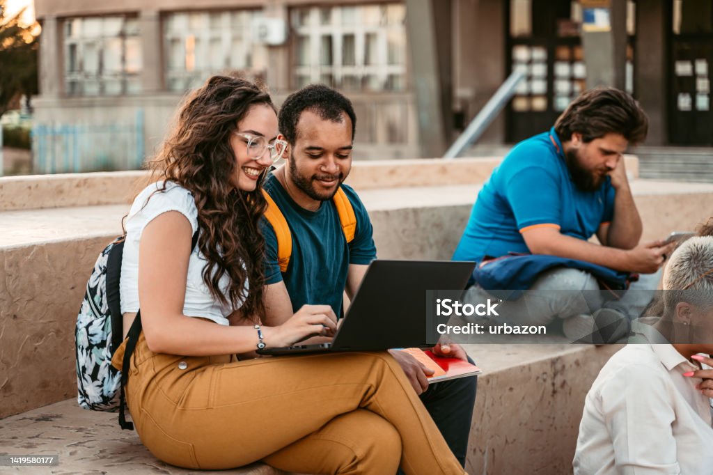Two Students Discussing Their Class Notes On The University Campus Two students discussing their class notes on the university campus, using laptop. Student Stock Photo