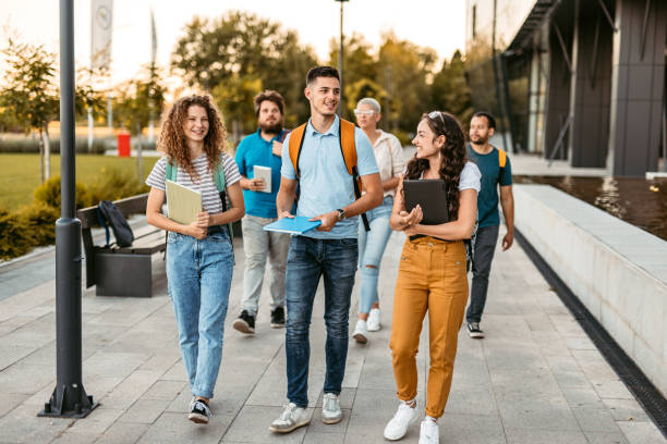 Students Walking  On The University Campus Group of friends walking on the university campus, holding books and notebooks. group of students stock pictures, royalty-free photos & images