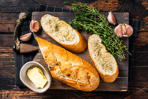 Toasted Garlic bread with herbs and butter on wooden cutting board. Wooden background. Top view.