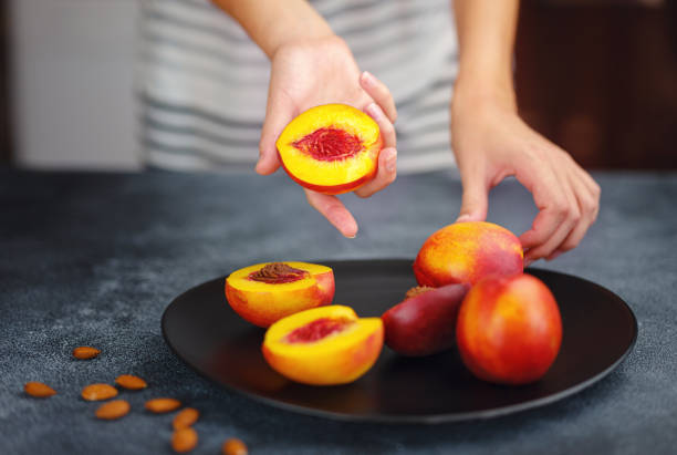 Hand holding fresh peach fruit and black dish stock photo