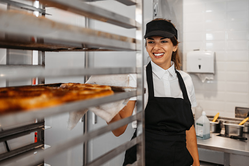 Beautiful young and happy female worker working in a modern bakery.