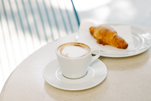 Cup of cappuccino and a croissant on a table in a street cafe. Selective focus. Place for text.