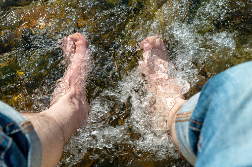 Flowing water between stones laps a man's feet in the sunshine in the summer