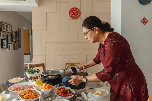 Chinese New Year - Senior Indian woman from a multi racial and multi generation family setting the table for reunion dinner