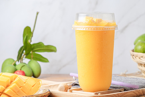Iced Mango Smoothie. in a clear plastic cup. Decorate Background with fresh mangoes. with space for Text.