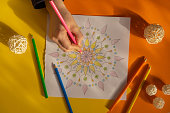 Female painting mandalas antistress page to combat stress. Relaxing hobby mental wellbeing and art therapy. Woman paints sketch, meditative process of coloring pages. Self expression by art