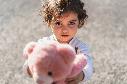 little female child gives her pink teddy bear looking to the camera - lifestyle concept of love and generosity in young children - or Mother's Day gift