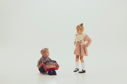 Portrait of little boy and girl, children in stylish clothes playing together isolated over grey background. Concept of childhood, friendship, fun, lifestyle, fashion, retro style, vintage