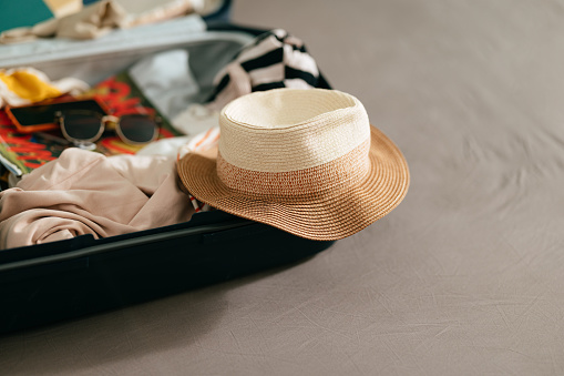 Cropped photo of a suitcase full of women's clothes for summer, a magazine, sunglasses, hat, books and a mobile phone.