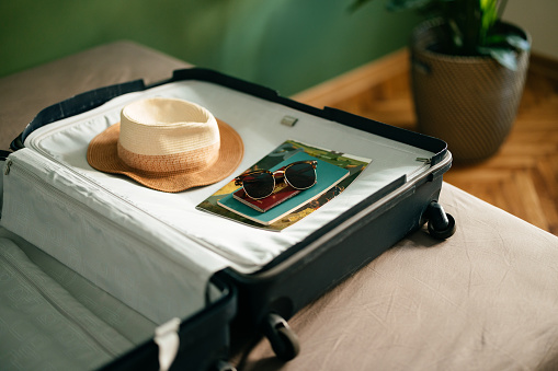 Close up shot of a hat, magazine, book, passport and sunglasses on top of a open suitcase ready to be packet for a summer vacation.