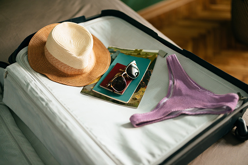 Close up shot of a hat, magazine, book, passport and sunglasses on top of a open suitcase ready to be packet for a summer vacation.