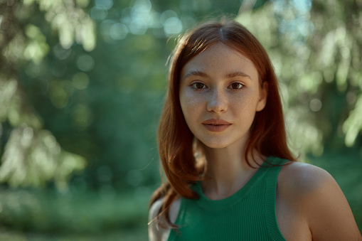 Close-up of pretty red-haired girl in the forest. Portrait of a young woman in a green top. High quality photo