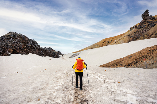 Hiker woman in yellow jacket trekking with travel expedition on snowy mountain in highlands of iceland at Landmannalaugar trail