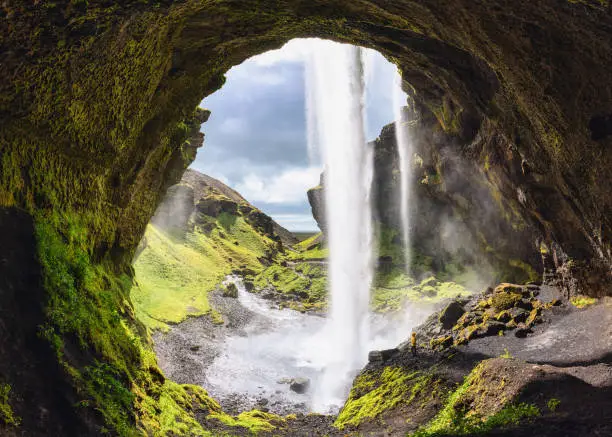 Photo of Kernufoss waterfall flowing from cliff and hiker standing in summer at Iceland