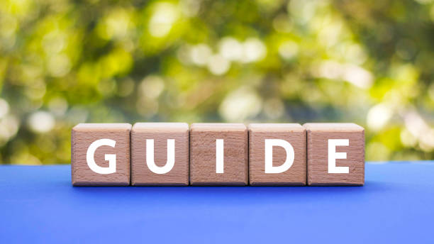 istock Text GUIDE on wooden cubes on blue table, blurred natural background. Square wood blocks. Top view, flat lay. 1419619409