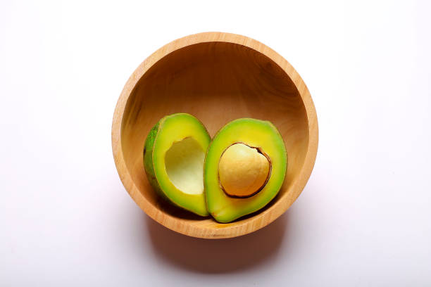 Avocado cut in half in a wooden bowl isolated on white background