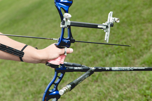 Hand of man with the bow, holding professional sports archery for competition on green grass background.