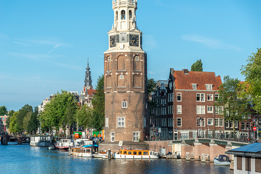 A peaceful panoramic morning view of Montelbaans Tower and the city reflecting in the canals of Amsterdam, Netherlands. Landscape, vivid urban scene.