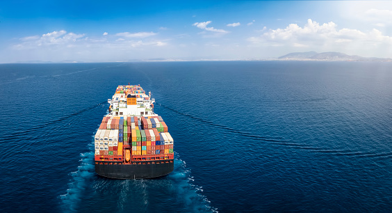 Panoramic back view of a cargo ship carrying containers for import and export, business logistic and transportation in open sea with copy space