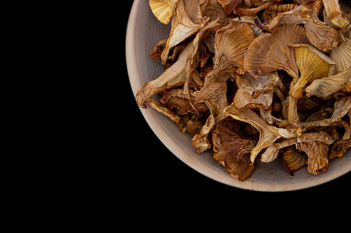 Close-up Dry Golden chanterelles in wooden bowl isolated on black background. Copy space, top view