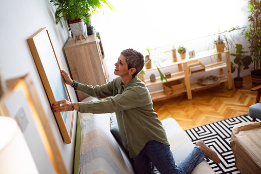 Woman decorating her home with a new painting.