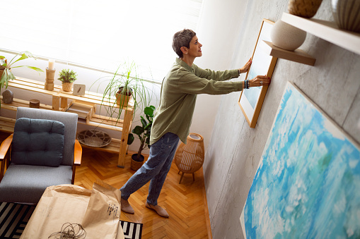 Woman decorating her home with a new painting.