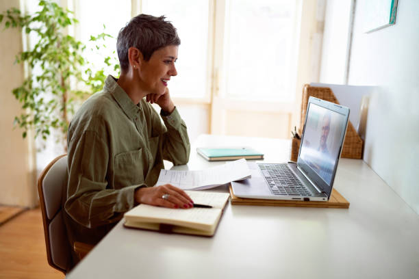 donna che segue corsi online sul suo laptop a casa - conferenza via web foto e immagini stock