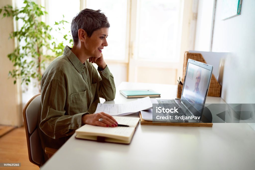 Woman following online courses on her laptop at home Woman following online courses on her laptop at home. E-Learning Stock Photo