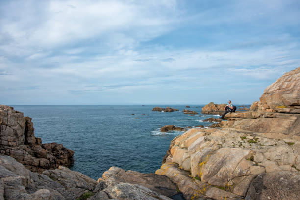 profile view of man standing on the edge of cliff on the coastline looking and admiring the view - hiking coastline waters edge sunny imagens e fotografias de stock