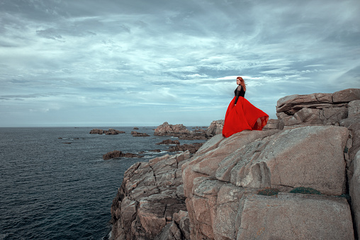 Side view woman wearing long red dress on the cliffs  beside the sea . Scenic view