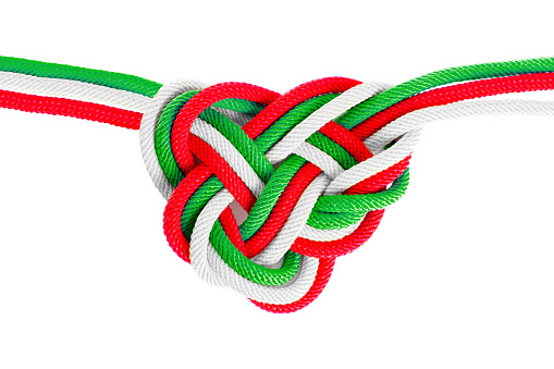 Heart-shaped celtic knot made from braided cords dyed red, green and white, isolated on neutral background. Creative eternity and friendship concept.