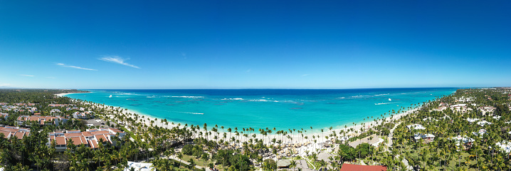 Bounty and pristine shore with resorts, palm trees, caribbean sea and people relaxing on beach. Tropical vacation. Dominican Republic. Aerial panorama view
