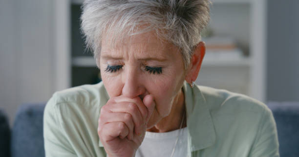 Covid, allergy or cancer, a senior woman with cough symptoms. Healthcare and medical insurance for medication, medicine or pills. Sick lady, on a sofa and in retirement, in pain and alone in her home stock photo