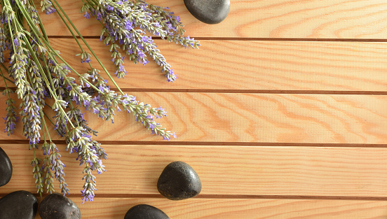 Wellness concept with black stonesand and spikes of flowering lavender on wooden table. Top view.