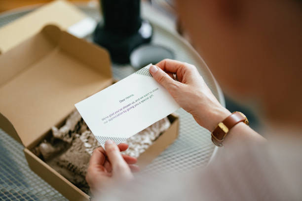 Anonymous Woman Reading a Note From a Gift Box (Copy Space) Anonymous woman sitting and in her hands  holding a paper note with a written message on it. There is an opened carton gift box on the coffee table in front of her and a cup of coffee. anonymous letter stock pictures, royalty-free photos & images