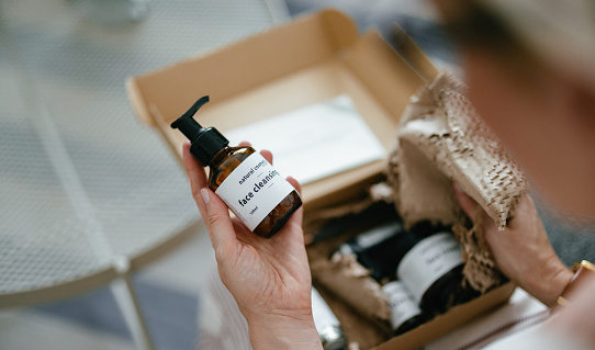 Anonymous woman holding a carton gift box on her knees. There are various natural beauty cosmetics products inside and a personal paper note.