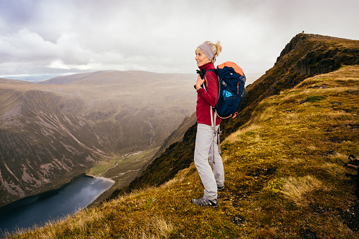 Woman near the summit of a Scottish Munro called Sgor Gaoith, near the resort of Aviemore, Scotland in summer. The ridge falls steeply through 500 metres of cliffs to the loch below.