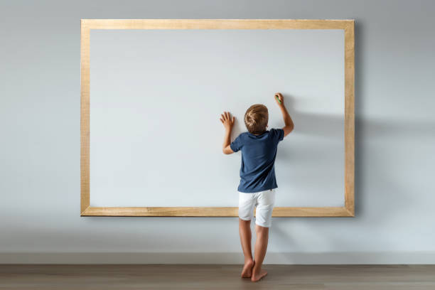 caucasian boy standing writing messages and texts on a large white board. mockup for inserting phrases and advertisements - blackboard teaching preschool alphabet imagens e fotografias de stock