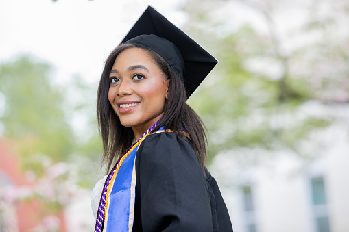 Young hispanic woman wearing graduated uniform holding diploma at university