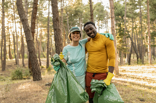 volunteer people collecting garbage in forest smiling, multiracial couple environmentalists.