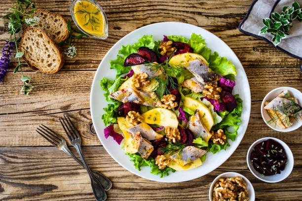 Marinated herring fillet with beetroots, apple, walnuts and greens on wooden black table Marinated herring fillet with beetroots, apple, walnuts and greens on wooden black table kipper stock pictures, royalty-free photos & images