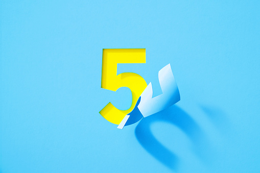 Blue number five folding on yellow background. Horizontal composition with copy space.